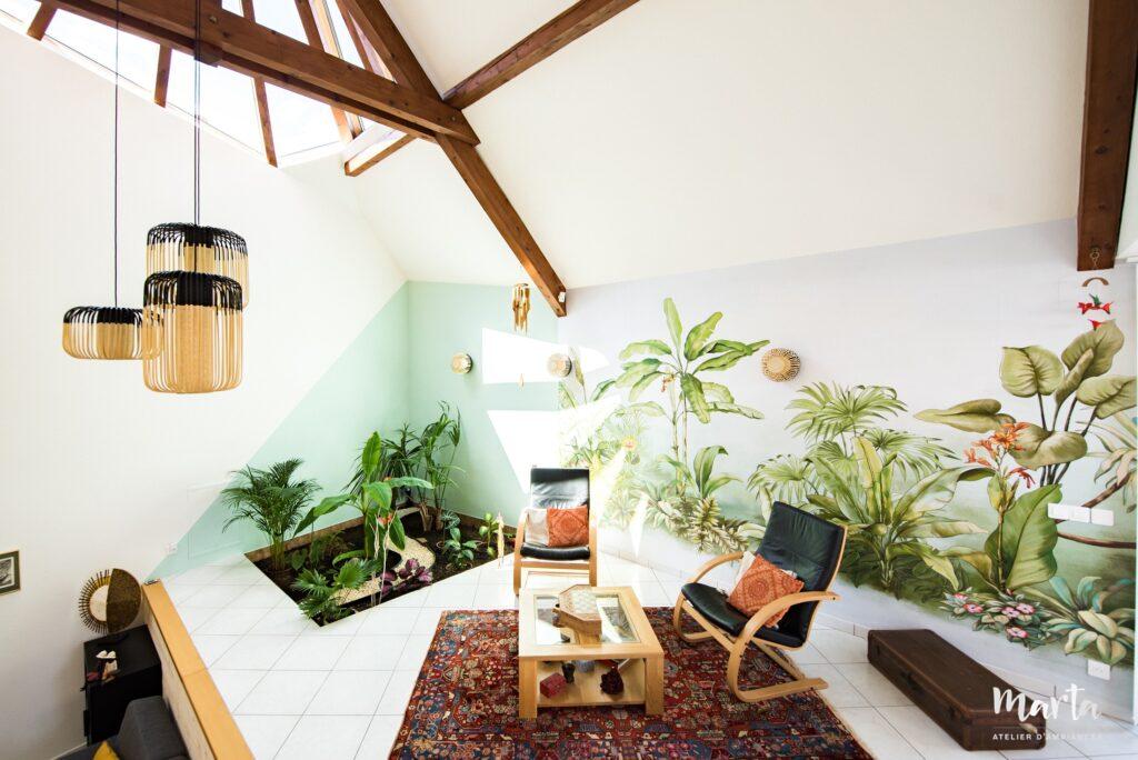 Deuxième salon avec fauteuils et table basse, panoramique jungle et jardin intérieur avec des palmiers plantés directement au sol, créant une ambiance exotique et naturelle